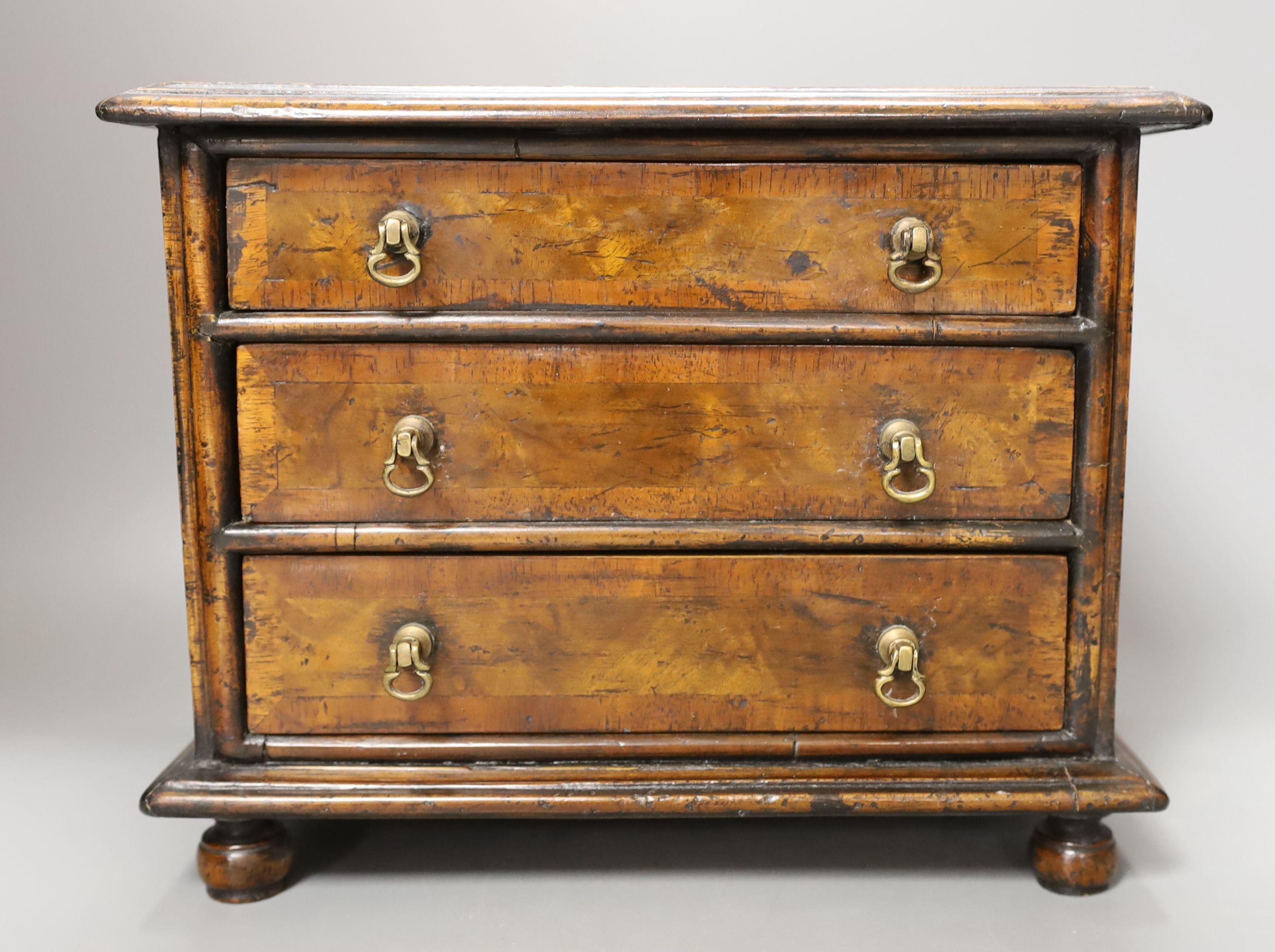 A cross banded walnut miniature chest of three drawers, 26cm wide